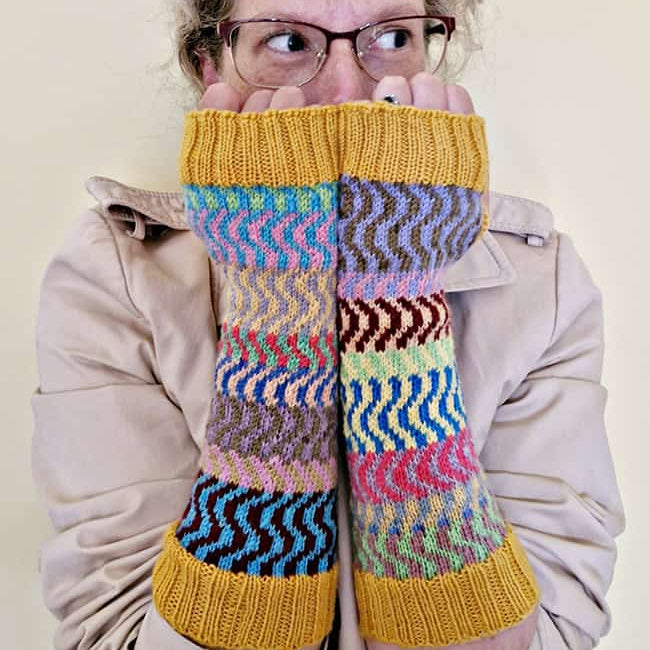 Person wearing colorful knitted arm warmers with a neutral background