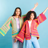 Two women wearing colorful crochet cardigans against a blue background